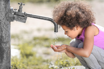 African American child drinking water from tap outdoors. Water scarcity concept