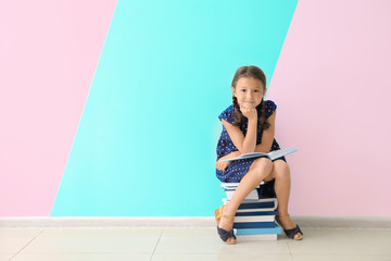 Cute little girl sitting on pile of books near color wall