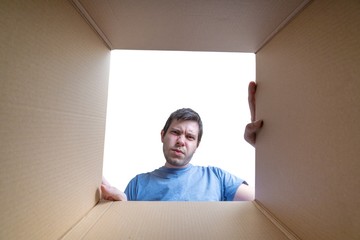 Young disappointed man is looking on gift inside cardboard box.