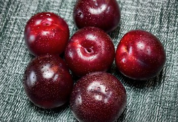 Fresh and ripe red plums with water droplets on a textile background.