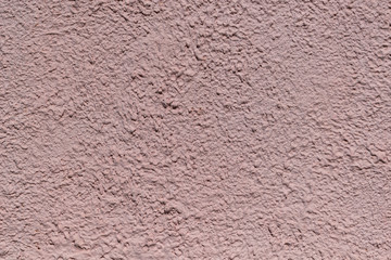 The rough texture of the decorative plaster on the wall. The surface of pink or beige with drips, drops and cracks. There are dimples and bumps.