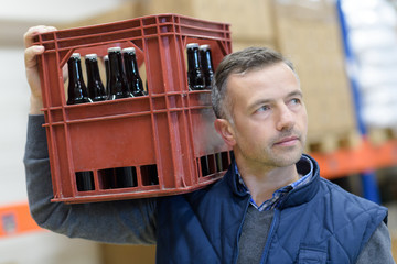 portrait of man holding beer bottles in crate at brewery