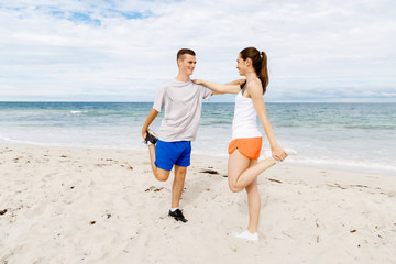 Runners. Young couple exercising and stertching on beach