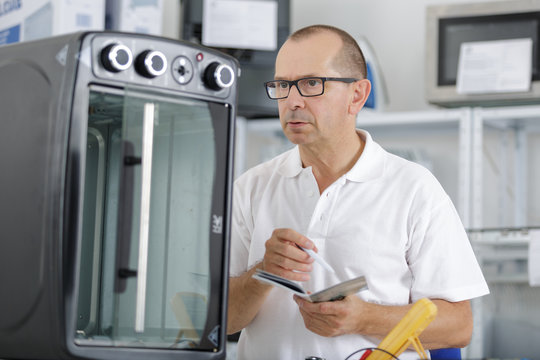 young repairman with screwdriver fixing kitchen oven