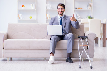 Businessman with crutches and broken leg at home working