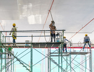 Naklejka premium Worker man painting a gypsum plaster ceiling with paint roller on the scaffold