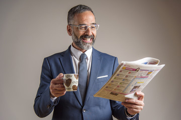 Happy senior business man reading newspapers and having his morning coffee