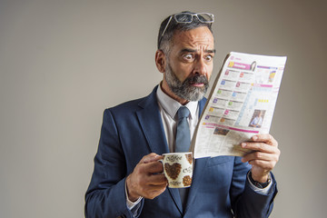 Worried and anxious senior business man looking at the newspaper with shock and terror on his face