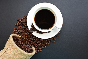 Roasted coffee beans and a cup of black coffee on black table, Top view