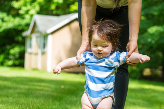 Baby boy learning to walk outside with the help of his parents
