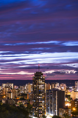 Fototapeta na wymiar Tall building and vibrant illuminated city beneath a dark blue and pink sunset sky