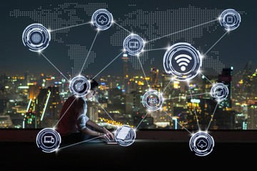 Asian businessman sitting and using the laptop showing the Wireless communication connecting of smart city Internet of Things Technology over cityscape background, technology business IOT concept