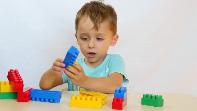 The boy collects the designer. The child builds from the colored blocks on the table.