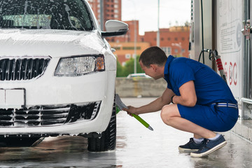 man washes a wheel, his car at a self-service car wash