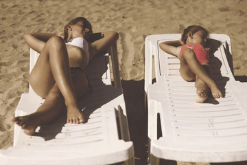 Mother and daughter sunbathing on the loungers on the beach.