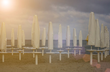 Folding beach umbrellas on a deserted beach during sunrise at seaside. Low season.
