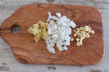 Chopped onions, ginger and garlic on an olive wooden cutting board.