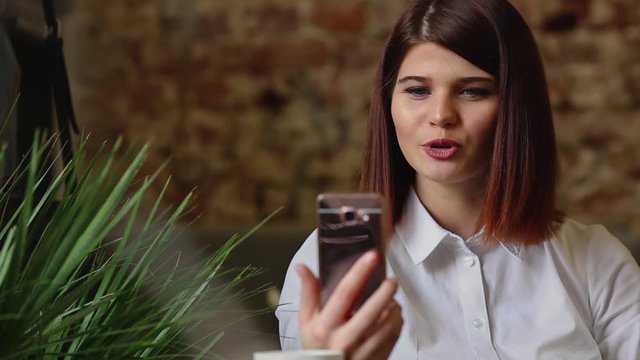 Smiling girl in cafe talking on the video chat on smart phone while drinking coffee