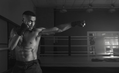 Fototapeta na wymiar Afro american male boxer. Young man boxing workout in a fitness club. Muscular strong man on background boxing gym. Black and white photo.