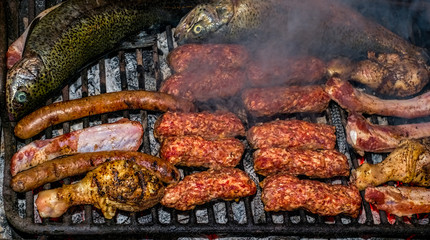 Barbecuing an assortment of meat with pork sausages, beef steak, chicken wings onions, tgrilled minced meat rolls and trout fish.