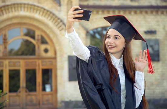 Woman on her graduation day. Use a smartphone while doing a self portrait photo. University, education, digital technology, mobile communication and happy woman - concept.