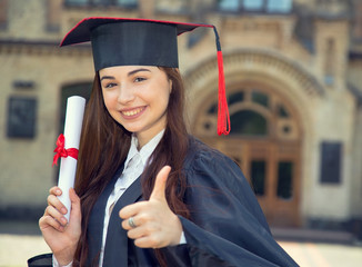 Happy graduate. Woman student in bachelor gown with diploma showing thumbs up.