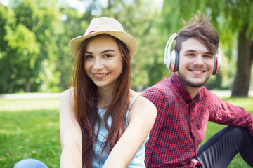 Portrait of a girl sitting next to the guy. Happy couple of young people having fun together on the green grass in the park campus.