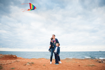 happy beautiful family consisting of mother and child playing kite standing on the ground near stormy sea in autumn