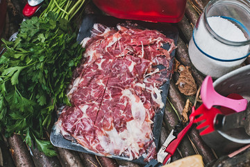 Jamon with greens on wooden table in woods.Selective focus/Jamon, parsley, salt and tourist cutlery on homemade wooden table in forest