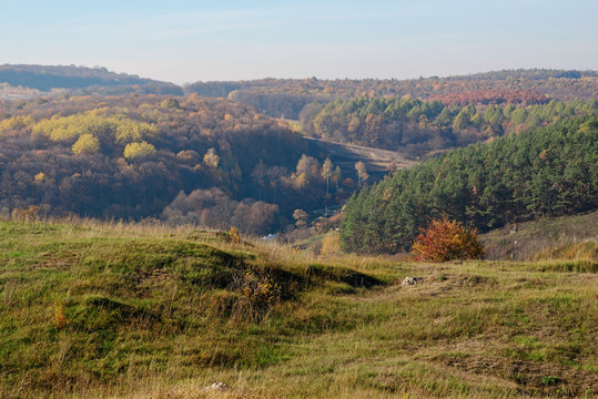 View on the beautiful colorful autumn landscape of the hills and greenfields with trees and grass upon the countryside