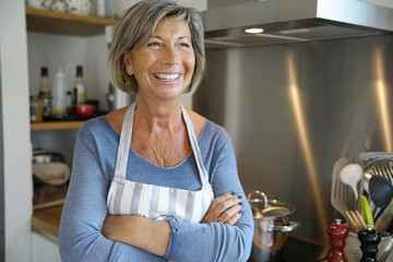 Cheerful Senior woman standing by stove in kitchen