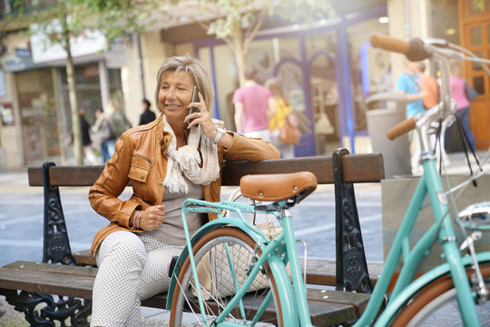 Senior woman in town with bike, talking on phone