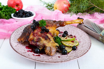 Baked goose leg in berry sauce on a ceramic plate on a white wooden background.
