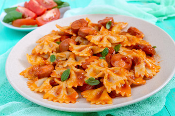 Farfalle pasta with chunks of sausage in tomato sauce on a bright background.