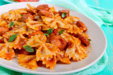 Farfalle pasta with chunks of sausage in tomato sauce on a bright background.