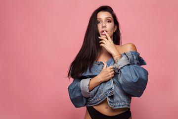 young gorgeous brunette model in jeans jacket, studio shot on pink background.