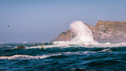 Racing Ocean Kayakers paddle their surfskis through breaking waves near the rocks
