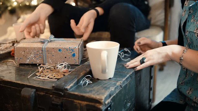 Close-up view of young couple sitting at the table, drinking tea and giving Christmas presents to each others.