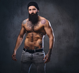 Shirtless muscular, bearded male holds dumbbell.