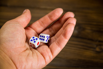 White dices in female hand against wooden table closeup