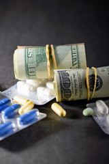 Money rolls and prescription drugs on dark table. Vertical image