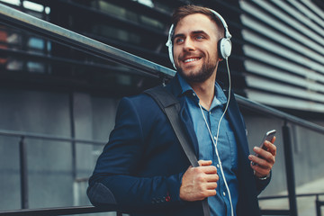Handsome young man listen to music via smartphone and headphones on the street
