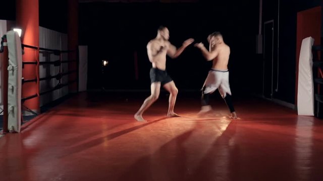 Two fighters spar in a dark lit gym. 