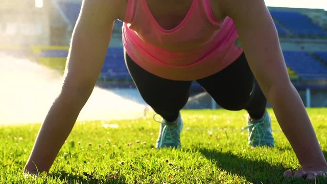 Fitness female doing pushups on green grass