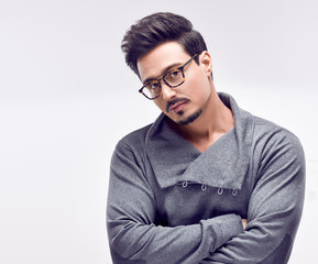 Handsome young Fashion guy. Autumn Trendy Outfit, Glasses. Sporty Confident Brunette Bearded man in fashionable gray jumper, Stylish Hairstyle. Studio fashion portrait on white background