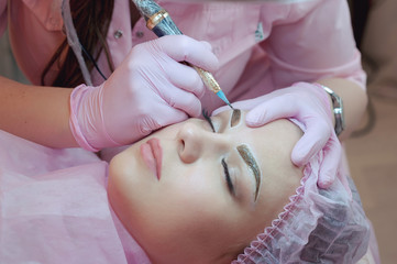 A young woman lies and gets a make-up of her eyebrows in a beauty salon. The use of permanent...