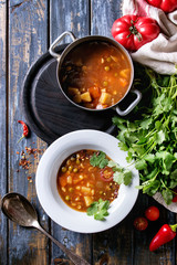 Vegetarian hot carrot tomato pea potato soup, served in plate and vintage aluminum pan with fresh coriander and tomatoes over old wooden plank table. Top view with space