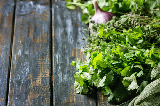 Variety of fresh organic herbs coriander, sage, oregano with garlic over old wooden plank background. Close up with space.