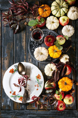 Autumn holiday table decoration setting with decorative pumpkins, apples, red leaves, empty plate with vintage cutlery, red wine, candle over wooden table. Rustic style. Flat lay