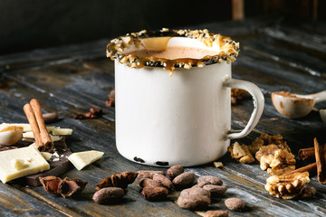 Vintage mug of hot chocolate, decor with nuts, caramel, spices. Ingredients above. Chopped dark and white chocolate, cocoa beans, anise over old wooden table. Dark rustic style